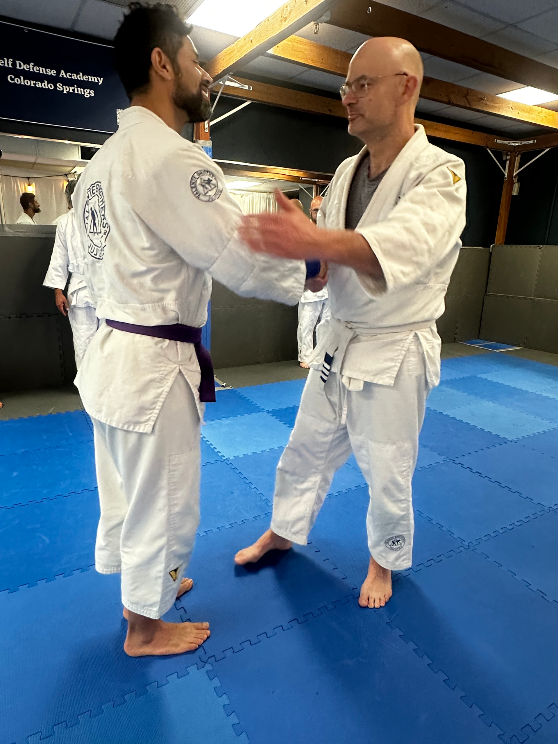 Jujutsu instructor Flip Aguilera practicing technique with student Mr. Daniel on blue mats at Self Defense Academy Colorado Springs
