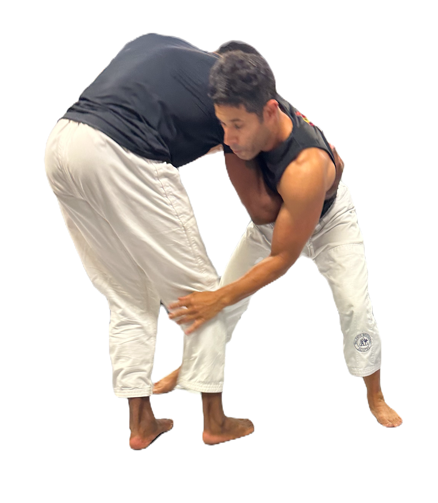 Two men grapple in a martial arts pose, wearing black tops and white pants, isolated on a black background.
